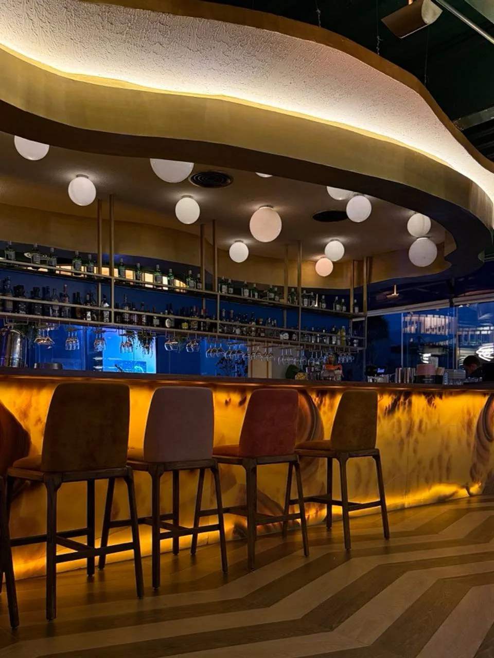 La barra: frente iluminado retroiluminado en ámbar bajo un plafón dorado.