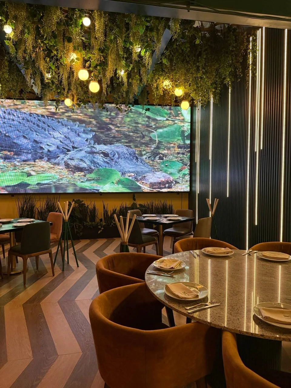 El muro de video del salón proyectando un cocodrilo bajo un dosel de plantas.