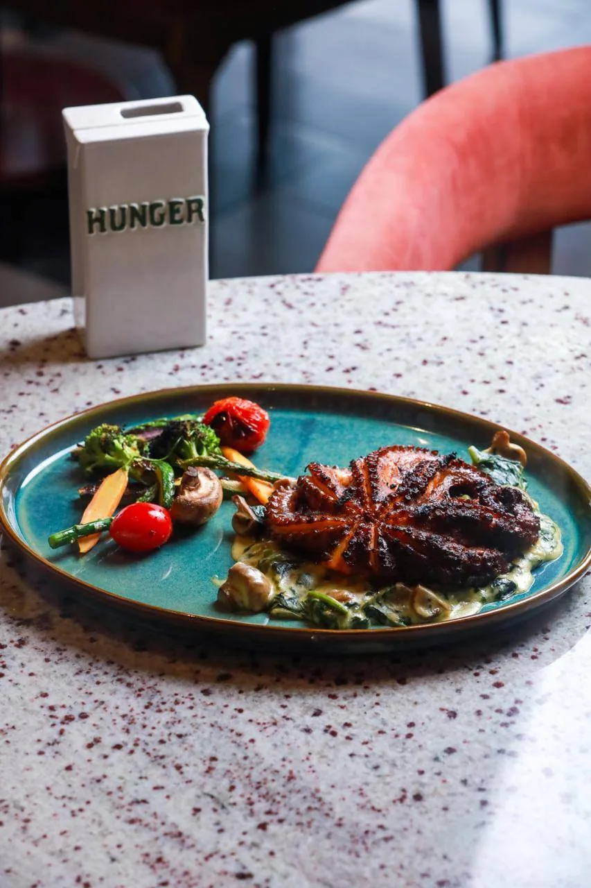 Pulpo adobado al Josper sobre plato de cerámica turquesa.