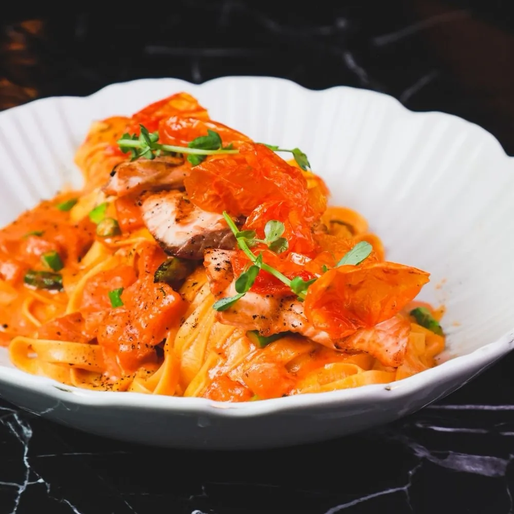 Fettuccine con salmón y jitomate confitado en plato acanalado.