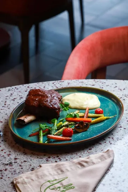 Short rib braseado con verduras al grill sobre plato turquesa.